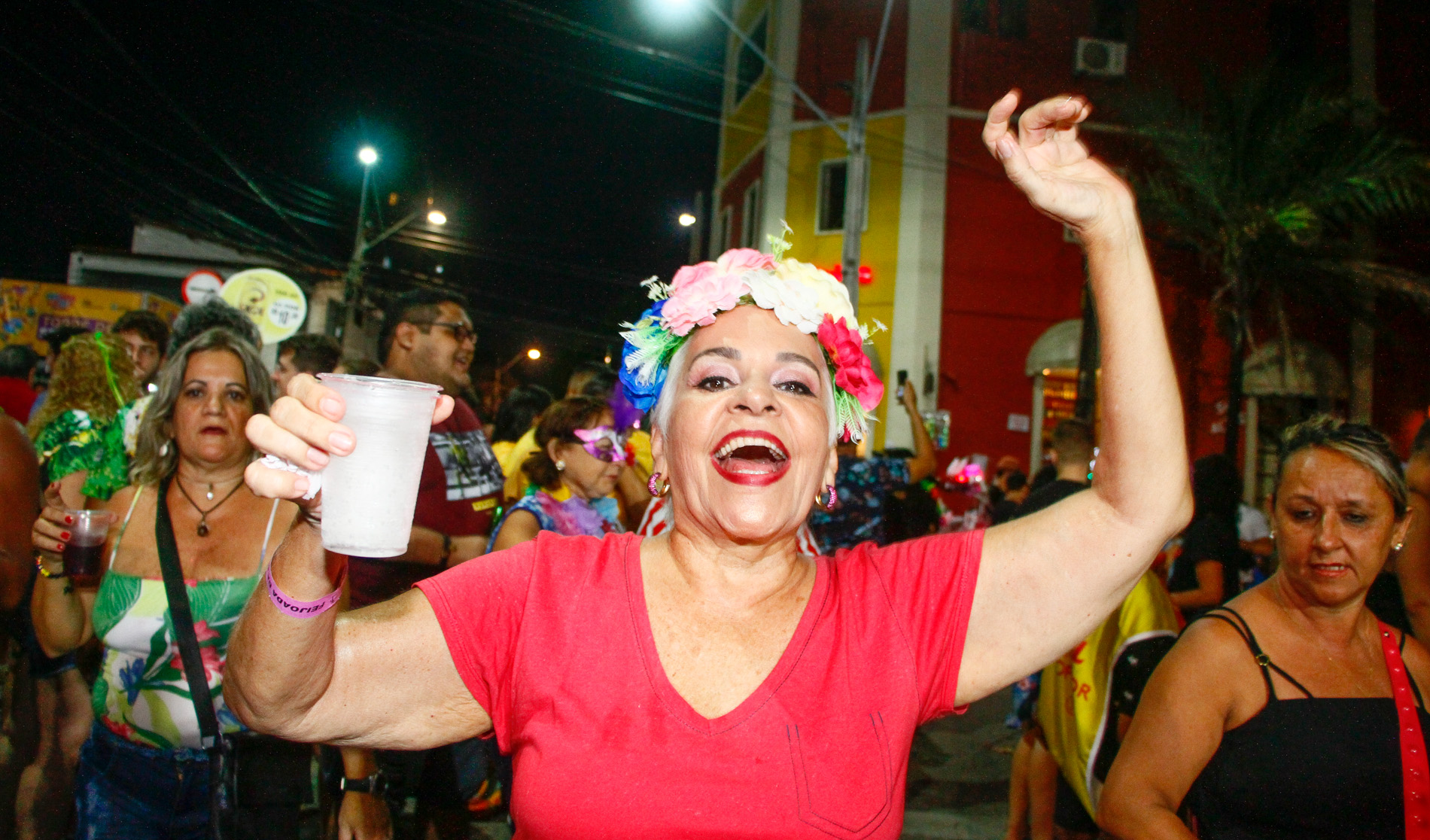 senhora sorrindo para a foto com braços para cima e flores na cabeça